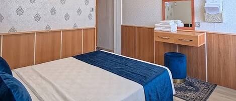 A hotel room with a bed, wooden paneling, a mirror, a small desk, and a blue rug.