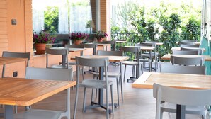 An outdoor café with tables and chairs, potted plants, and a view of greenery. - Hotel Ariston (Imperia)