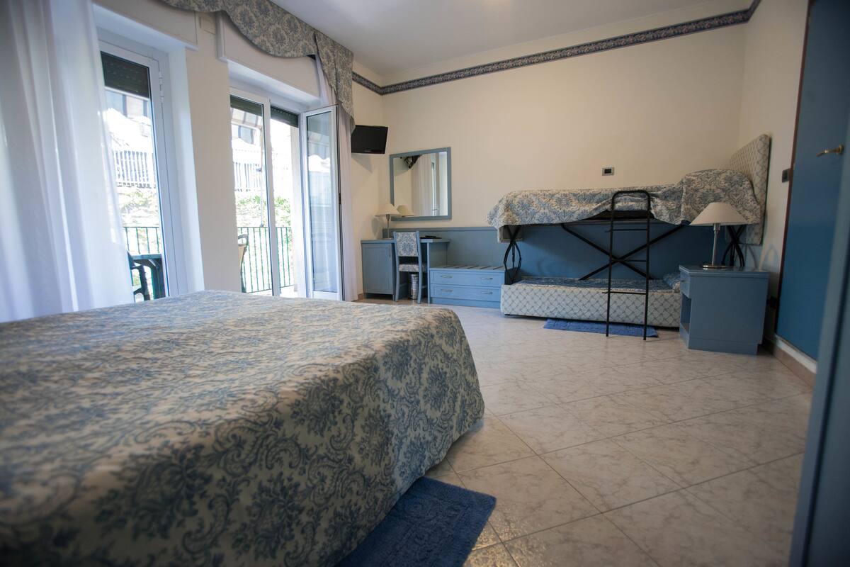 A bedroom with a bed, a desk, a chair, a dresser, a mirror, and a window.