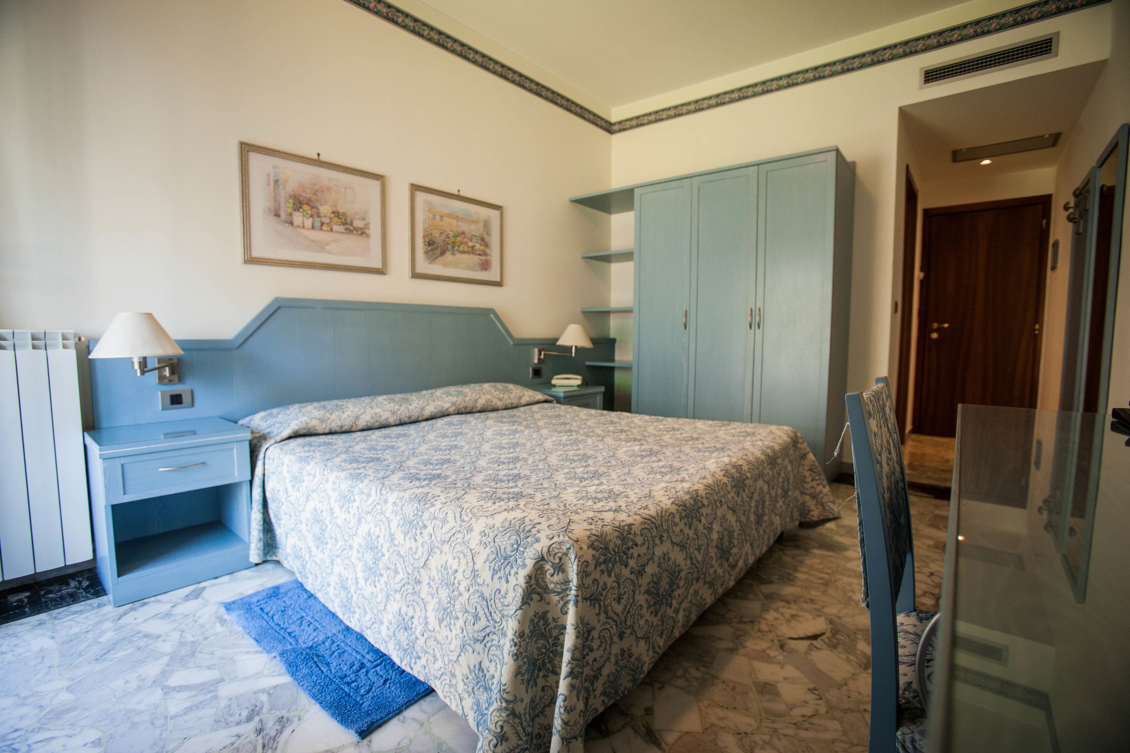 Een slaapkamer met een bed, nachtkastje, dressoir en een deur naar een andere kamer.