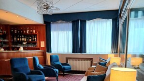 A hotel lobby with a bar area, seating with blue armchairs, a sofa with orange cushions, and a large window with curtains. - Hotel Ariston (Imperia)