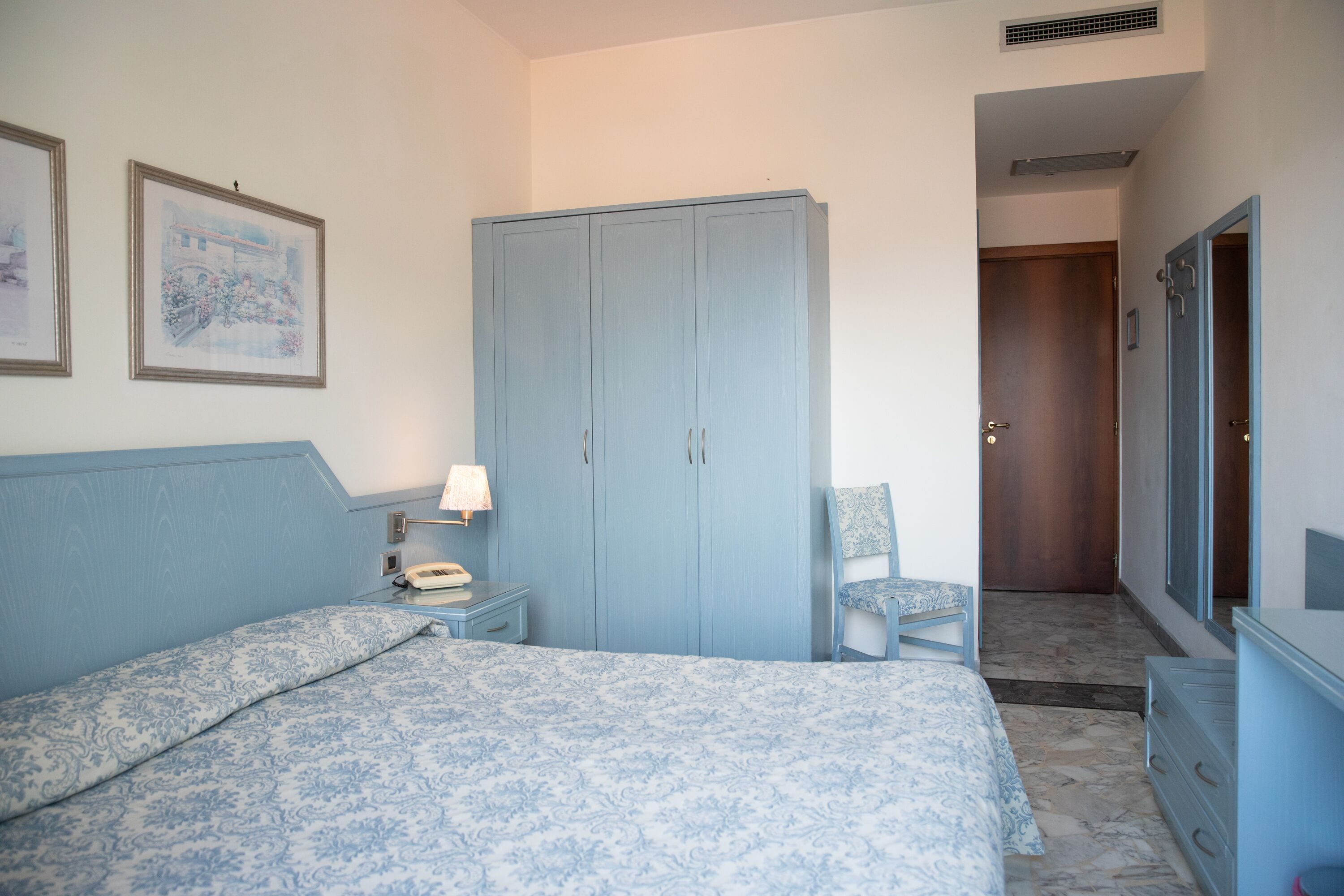 Un dormitorio con cama, armario, silla y escritorio con lámpara.
