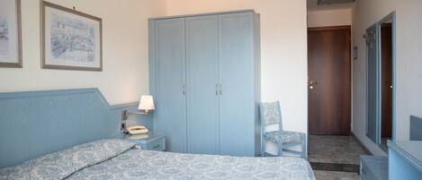 A bedroom with a bed, a wardrobe, a chair, and a desk with a lamp.