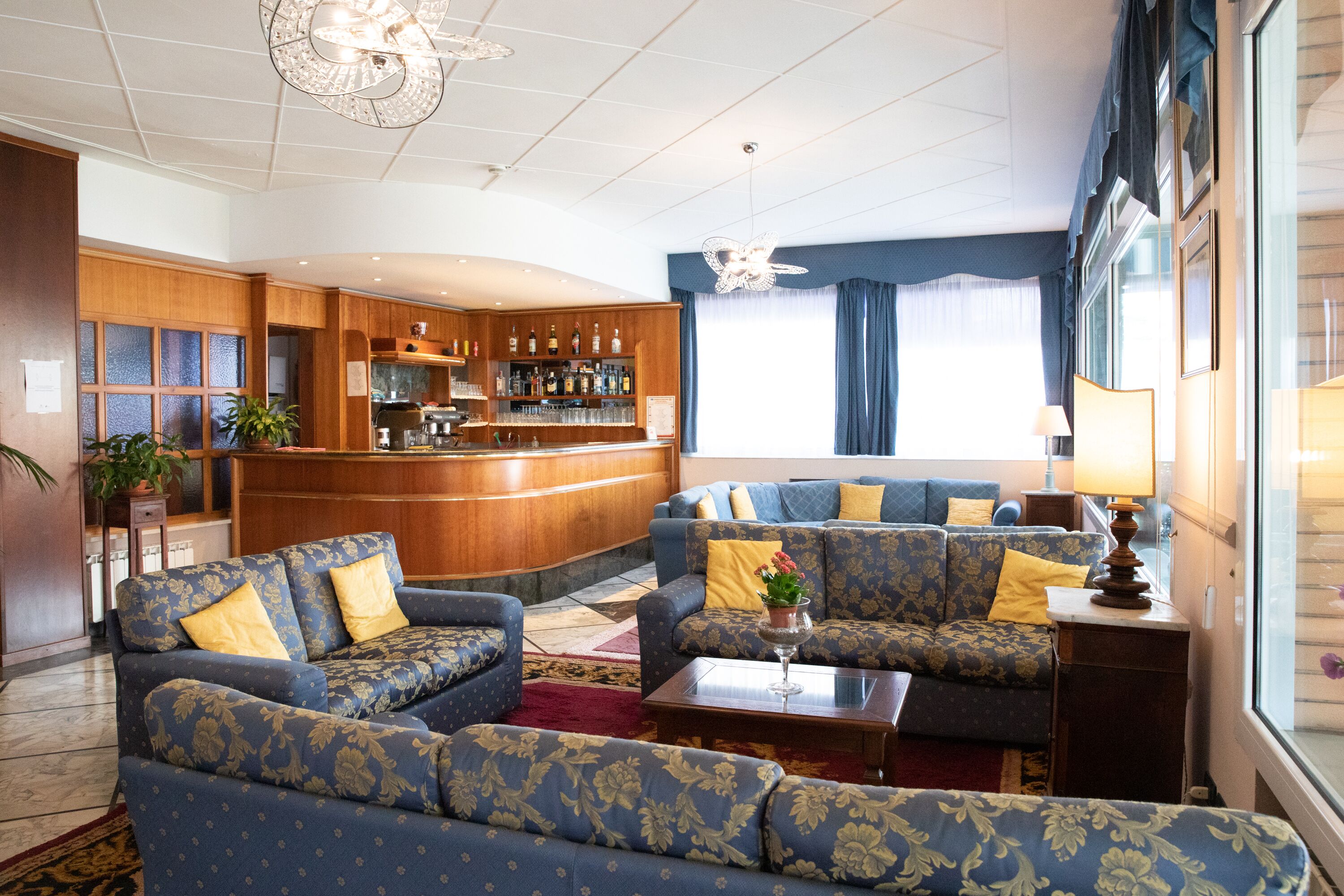 A hotel lobby with a bar area, sofas, and a large window with curtains.