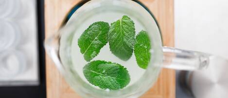 Una taza de vidrio transparente con hojas de menta flotando sobre una superficie de madera.