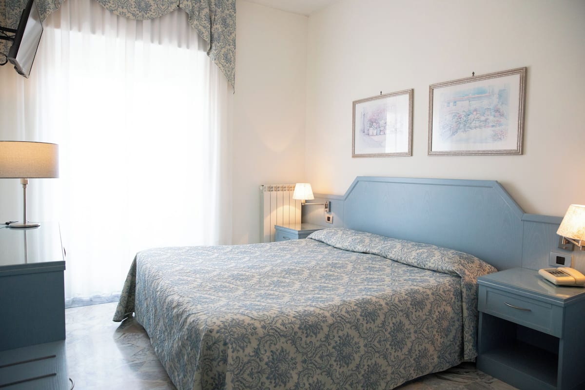 A bedroom with a bed, nightstands, a lamp, and two framed pictures on the wall.