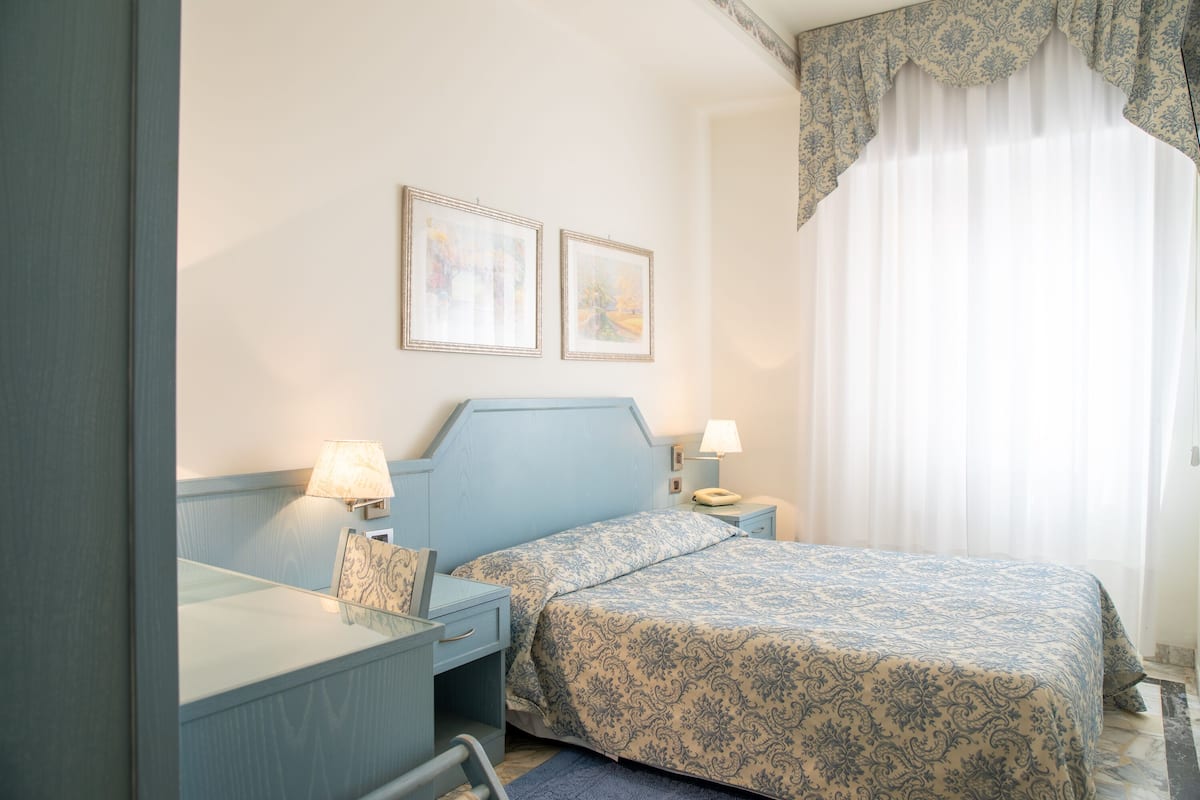 A bedroom with a bed, bedside tables, lamps, and two framed pictures on the wall.