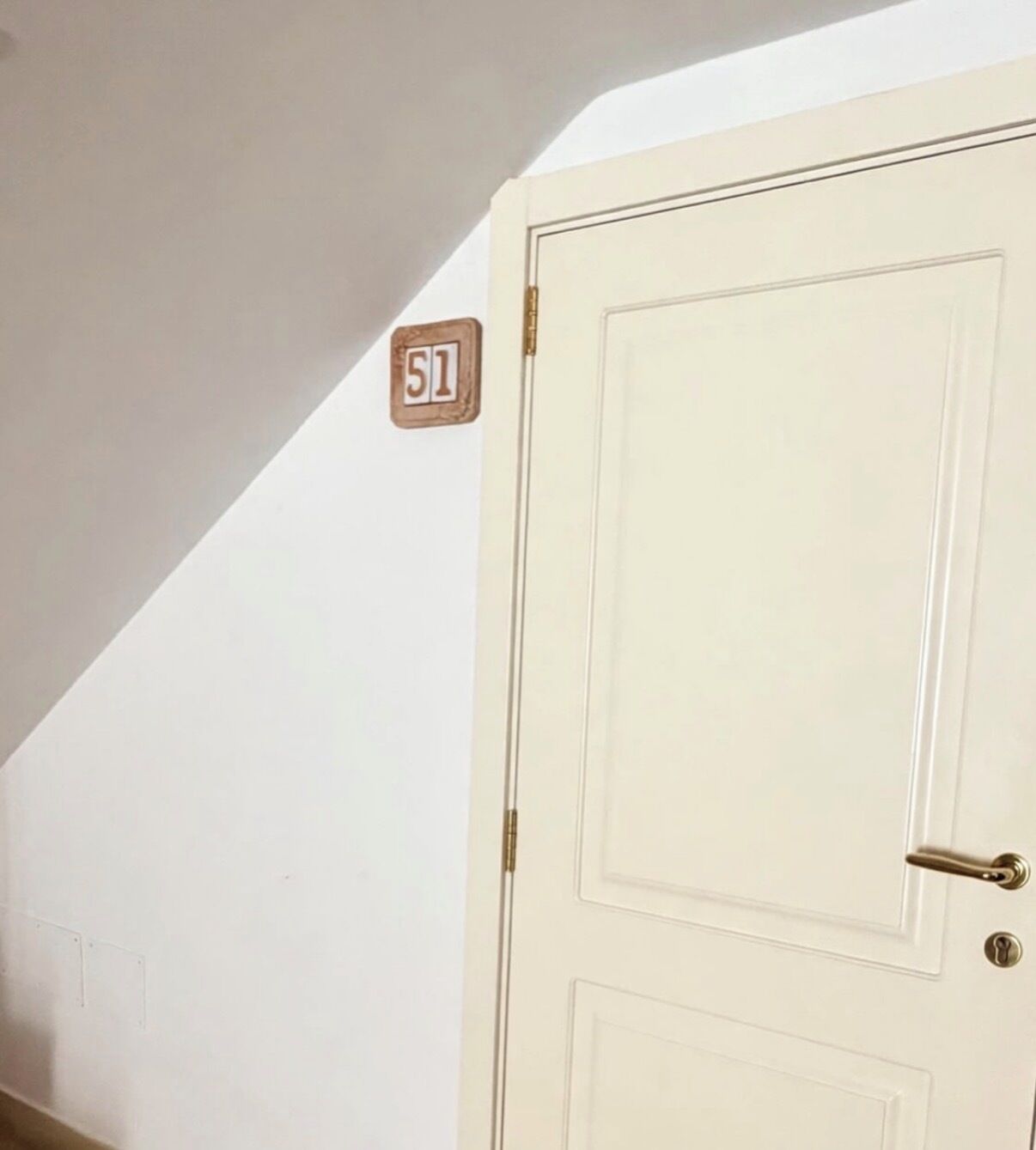 Une porte blanche avec une poignée en laiton et une petite plaque en bois portant le numéro « 51 », fixée au mur juste au-dessus.