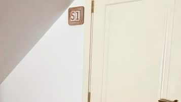 Une porte blanche avec une poignée en laiton et une petite plaque en bois portant le numéro « 51 », fixée au mur juste au-dessus.