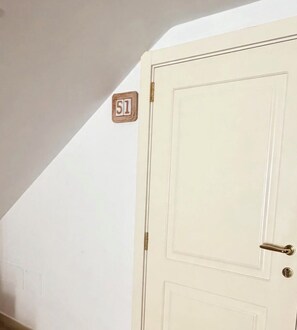 Een witte deur met een messing handgreep en een klein houten bordje met het cijfer '51' erop, bevestigd aan de muur erboven.