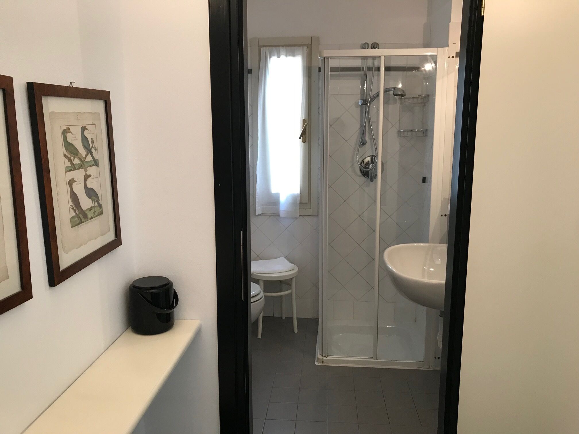 A bathroom with a glass-enclosed shower, a white sink, and a small white stool.