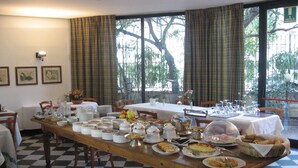 A dining area with a checkered floor, a long table set with various dishes, and a view of trees through large windows.