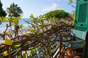 Un balcón con vista a la playa, que incluye una silla de madera y una pared con persianas verdes.