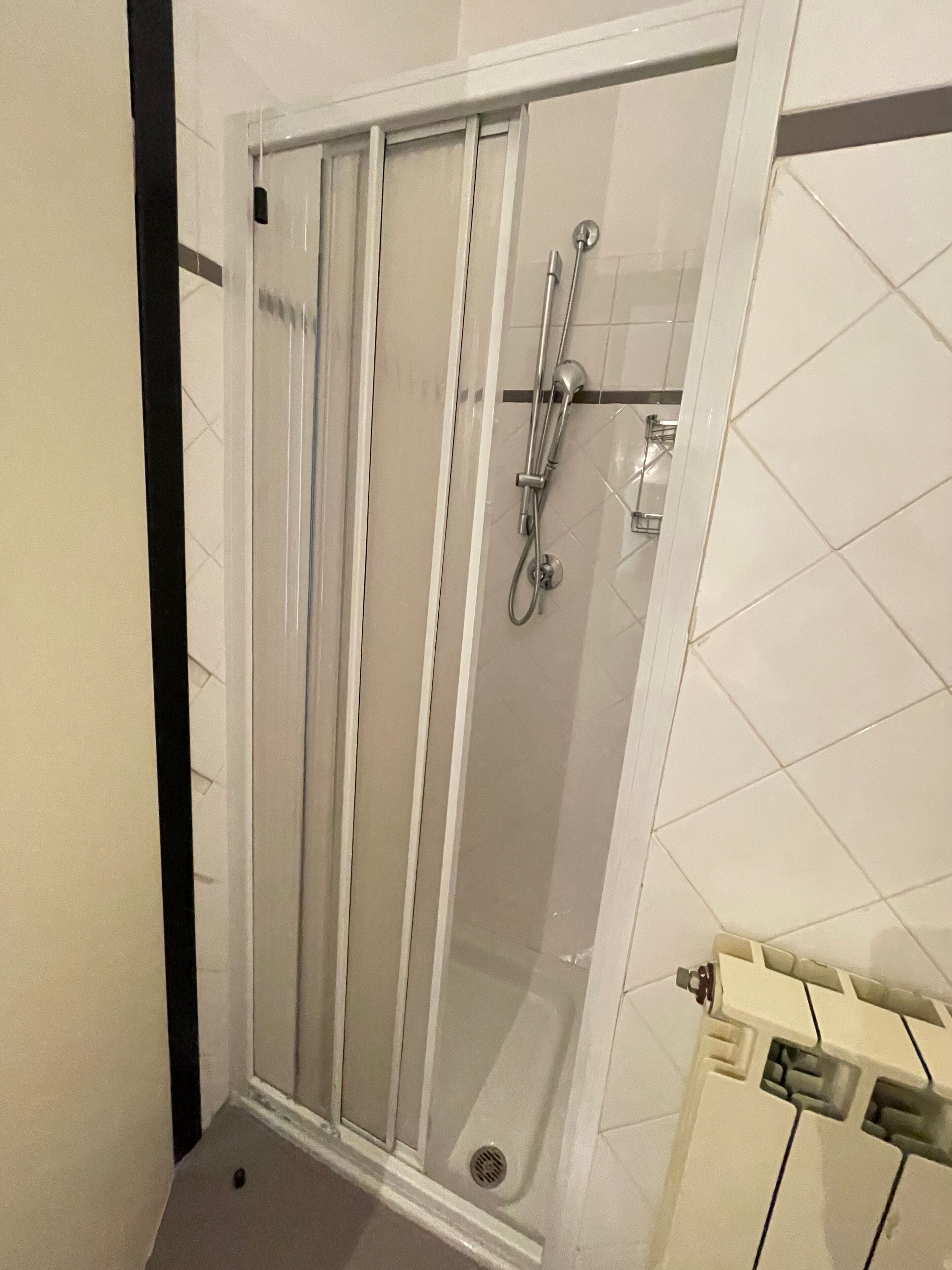 A shower with a glass door, a handheld showerhead, and a wall-mounted faucet.