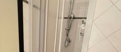 A shower with a glass door, a handheld showerhead, and a wall-mounted faucet.