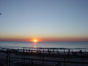 A sunset over a beach with a railing in the foreground.