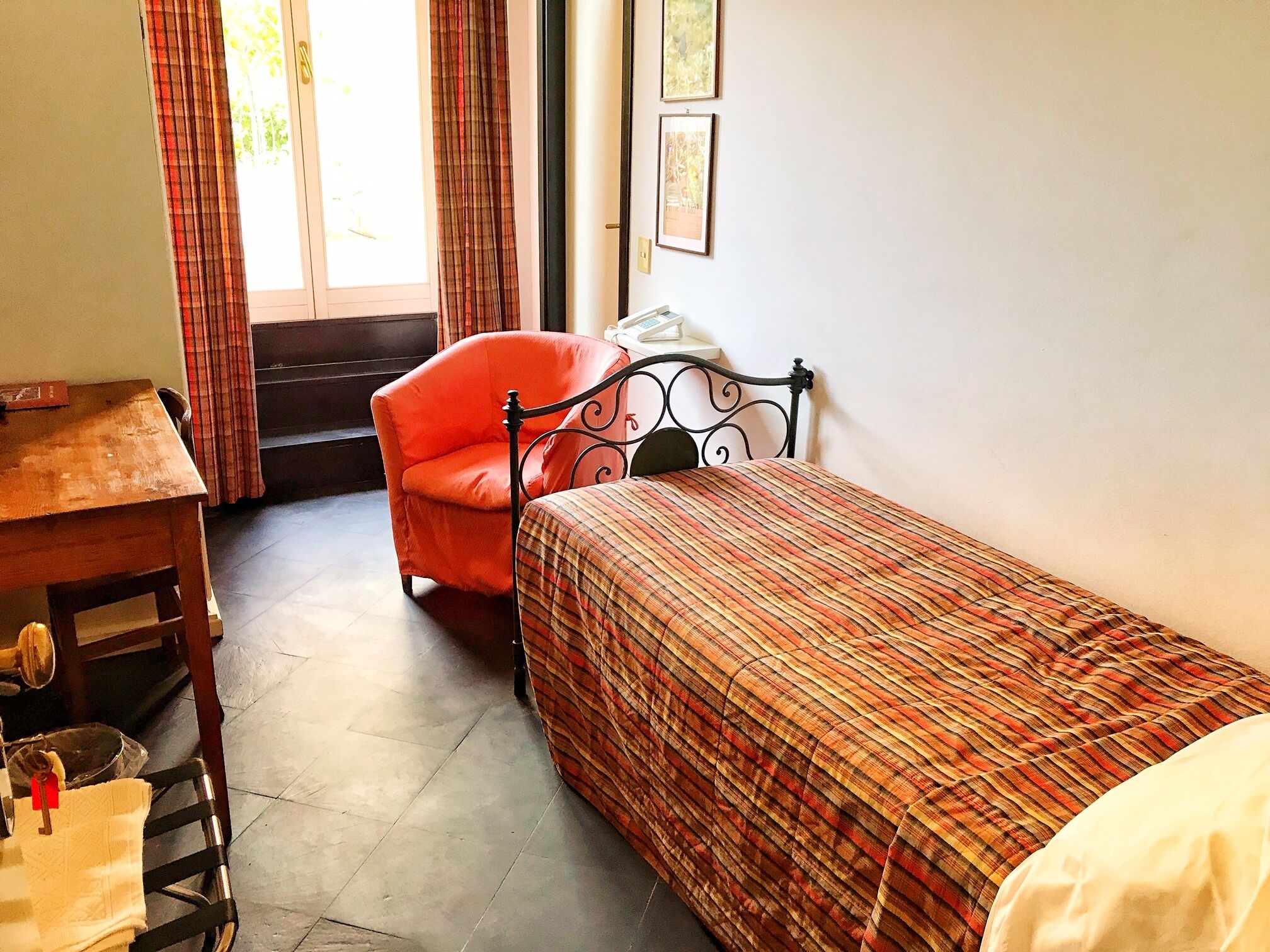 A small room with a single bed, a chair, a table, and a window with curtains.
