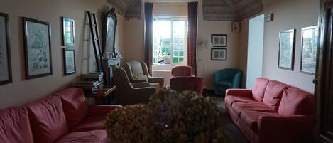 A living room with two red sofas, a coffee table, and a vase of flowers. There are framed pictures on the walls and a window with curtains.