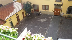A courtyard with a yellow building, a wooden door, and a motorcycle parked in the center. - Maison de Charme (Florence)