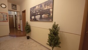 A hallway with a large painting of a bridge, a clock, and two potted plants. - Maison de Charme (Florence)