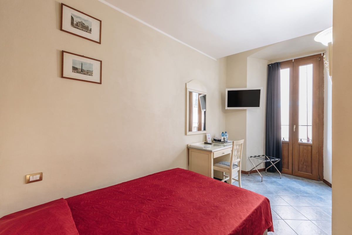 Una habitación de hotel con cama, escritorio, silla y televisor montado en la pared.