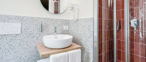 Un baño con un espejo redondo, un lavamanos blanco y una zona de ducha con azulejos rojos.