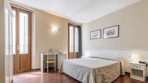 A bedroom with a large bed, a desk, a chair, and two bedside tables with lamps. - Hotel Astoria (Cremona)