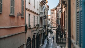 A narrow street with buildings on either side, featuring balconies and arched doorways. - Hotel Astoria (Cremona)