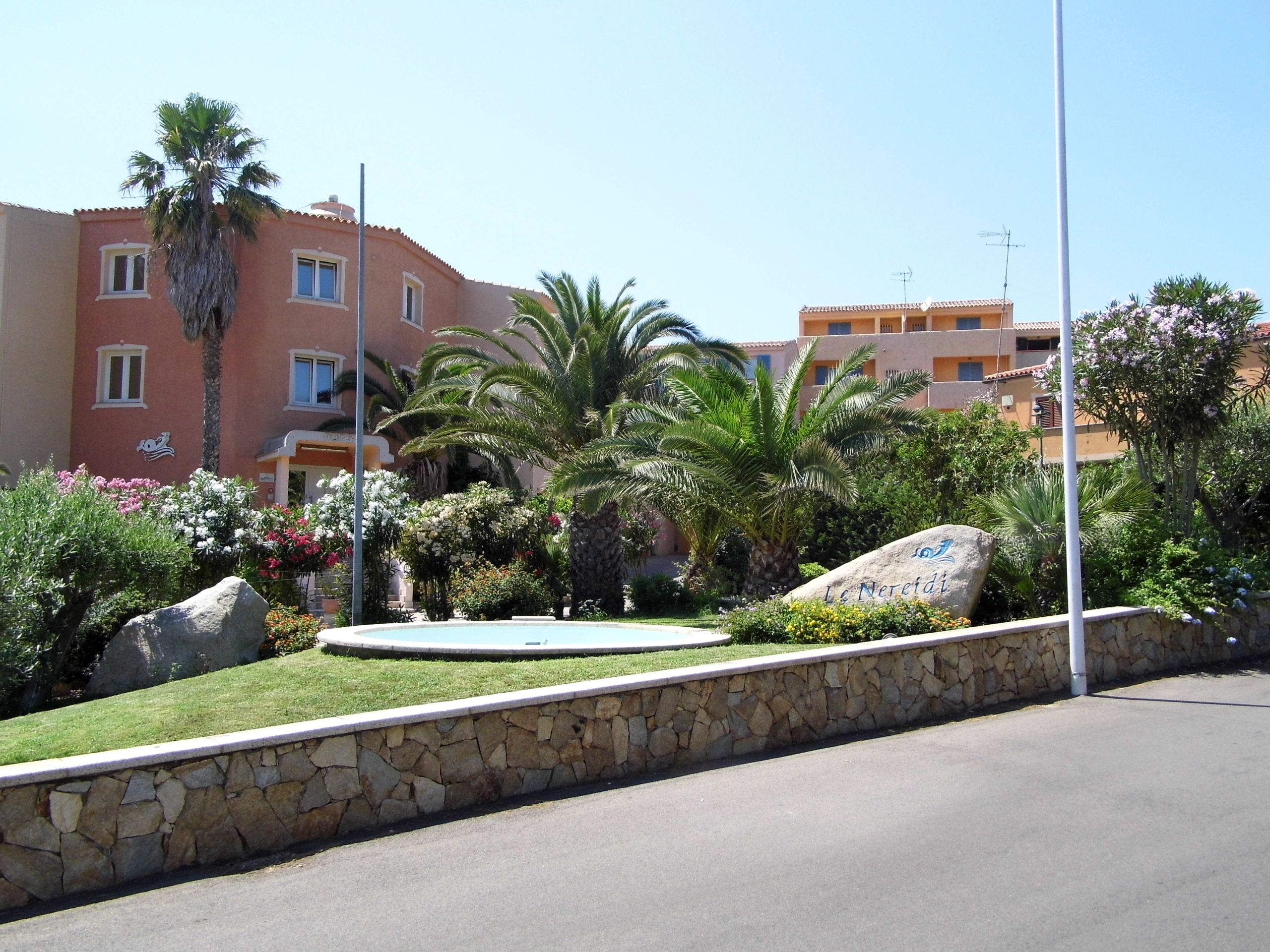 Un hotel con pared de piedra, palmeras y cielo despejado.