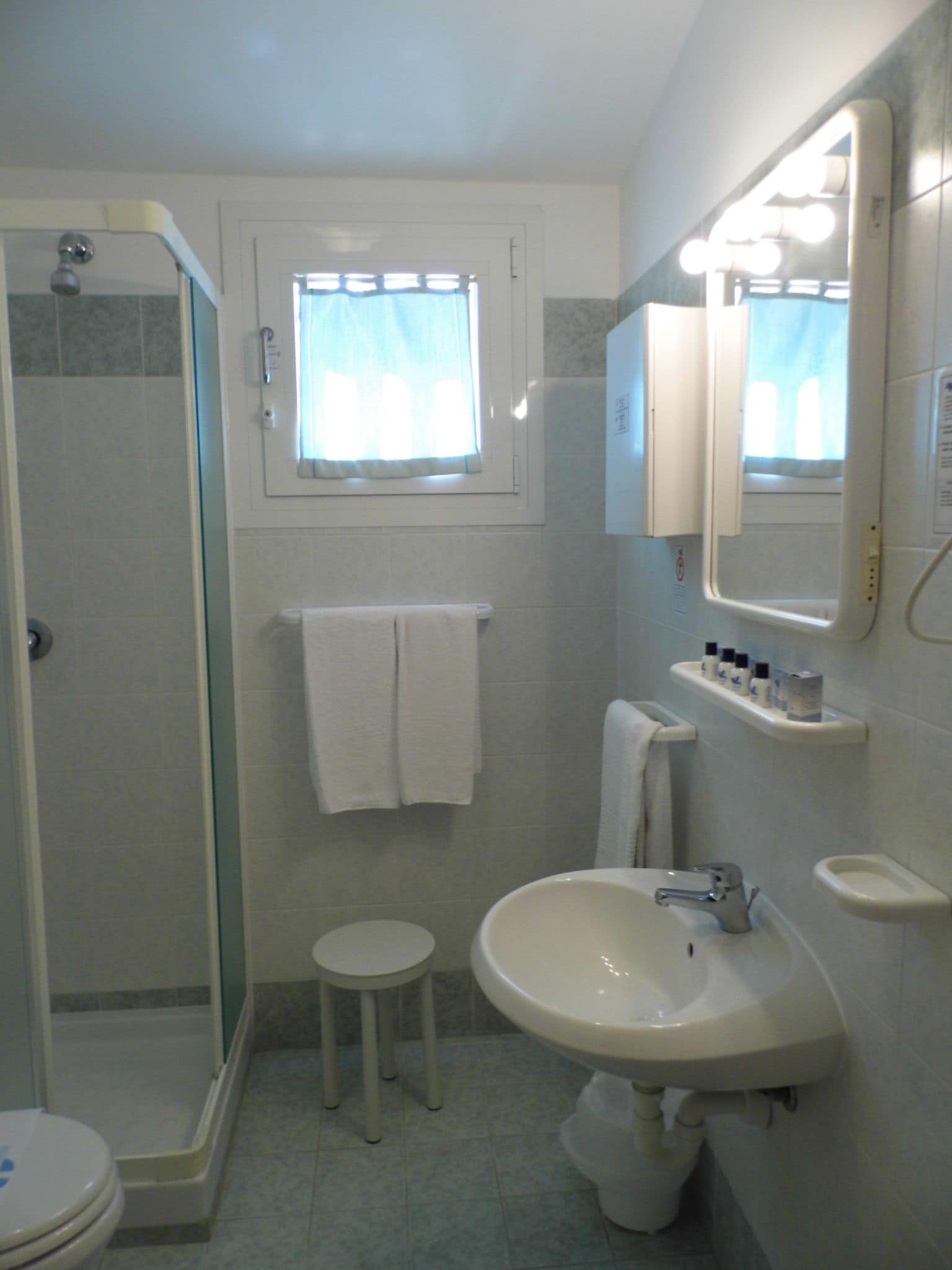 A bathroom with a shower, toilet, sink, and a window with curtains.
