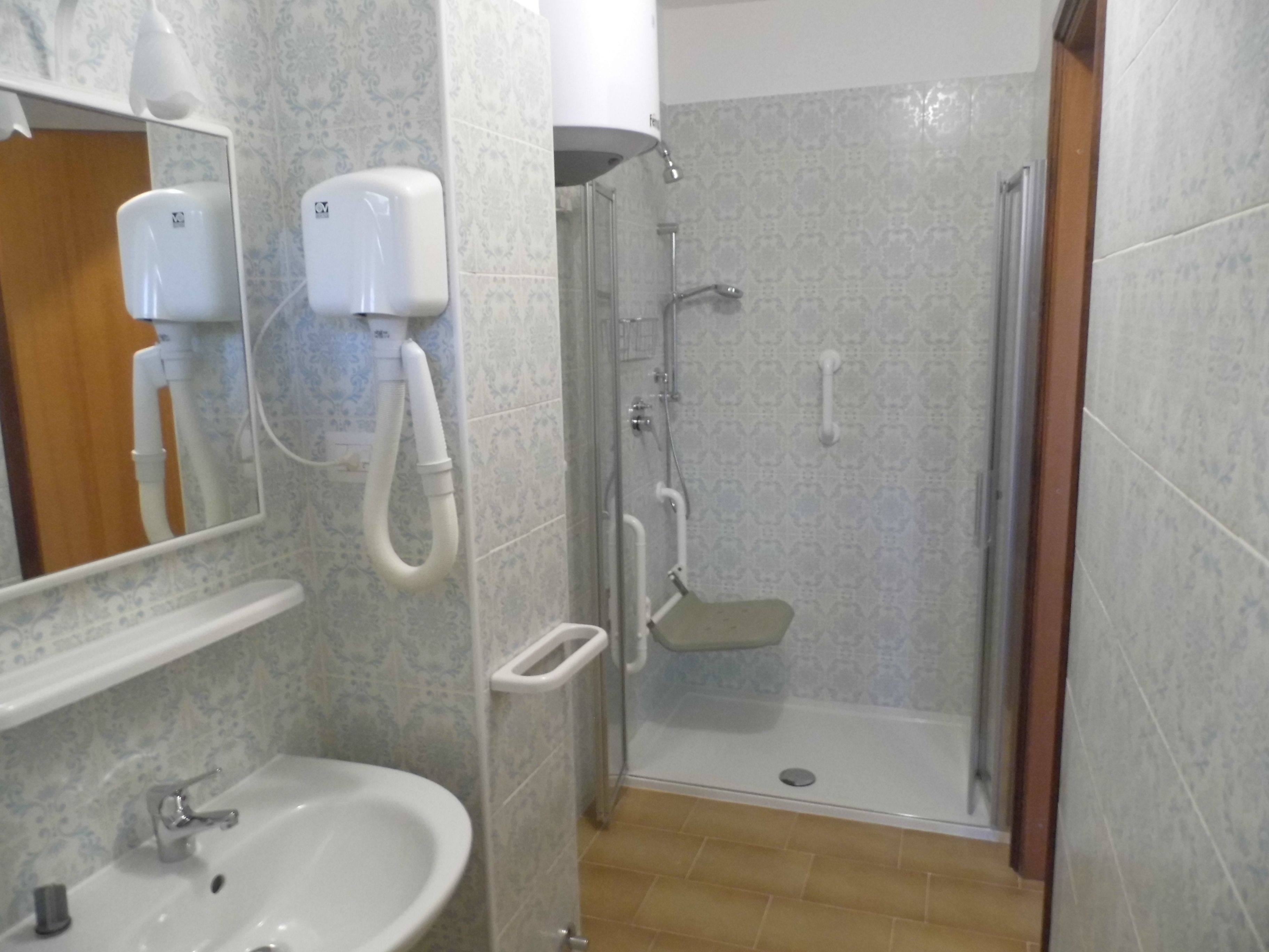 A bathroom with a sink, mirror, hand dryer, and a glass-enclosed shower area.