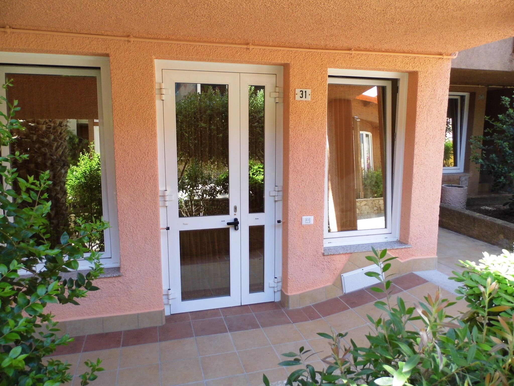 Ein Gebäude mit hellbeiger Fassade, einer Doppeltür mit Glasfenster und einem Fenster mit Vorhang.