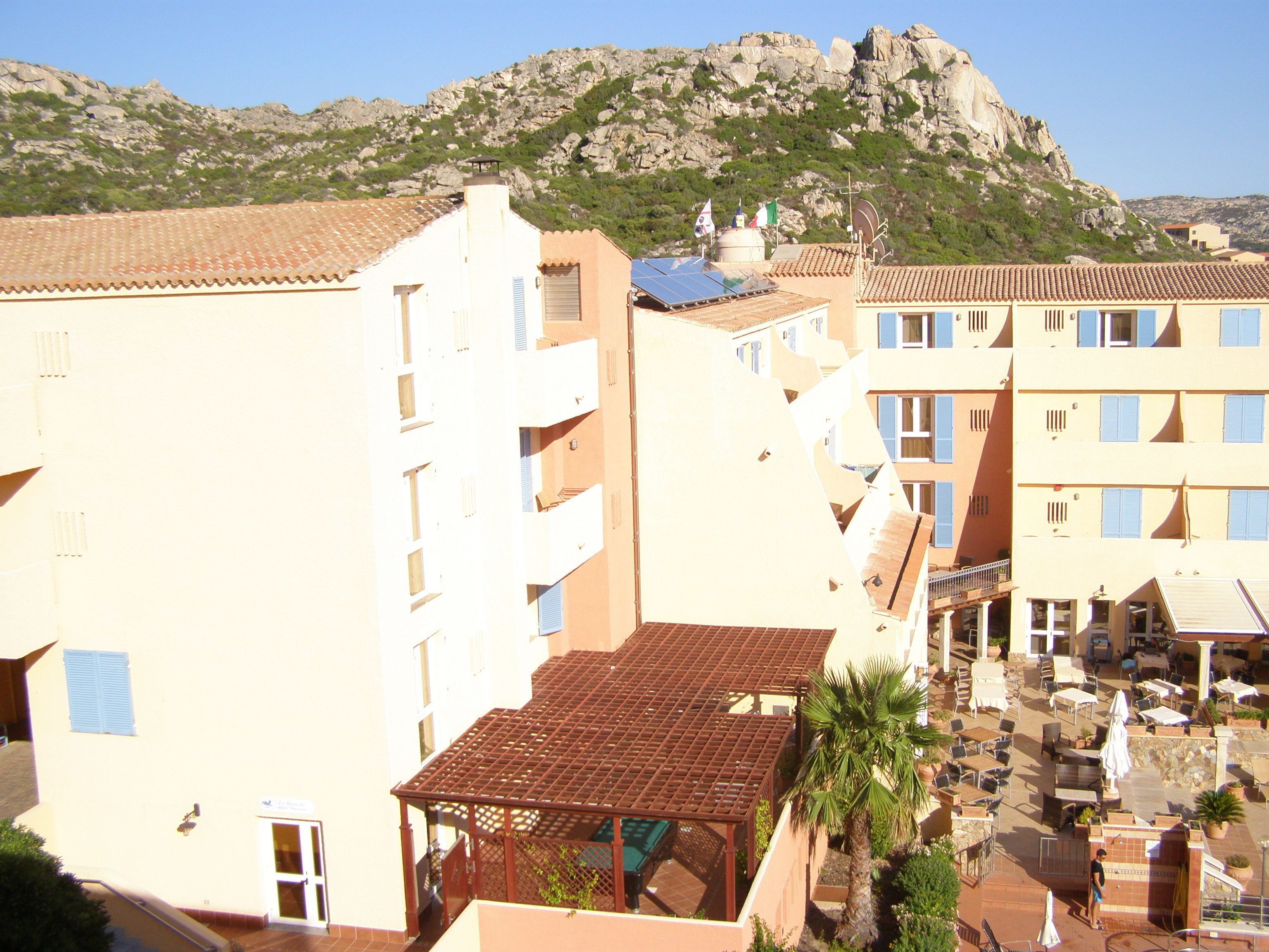 Un hotel de varios pisos, con zonas de estar al aire libre y montañas al fondo.