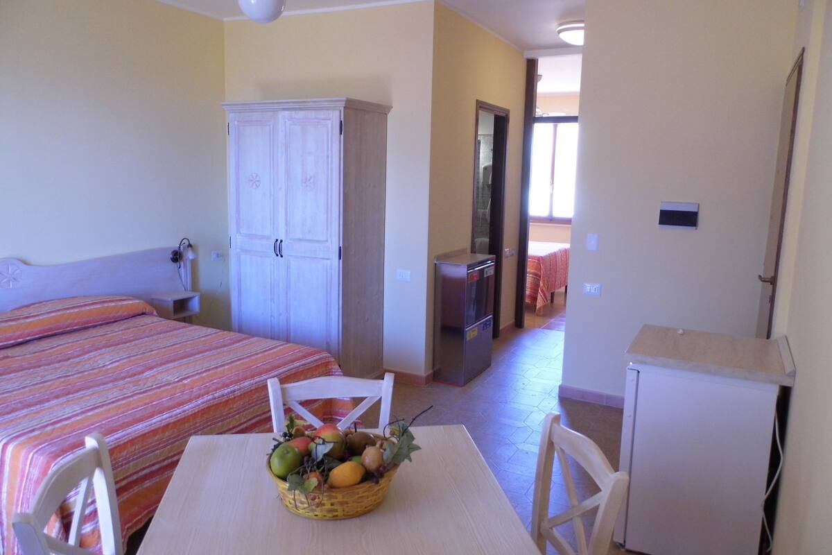 Habitación de hotel con cama, escritorio con cesta de fruta, armario y un refrigerador pequeño.