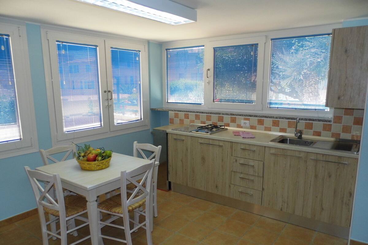 Una cocina con una mesa de comedor, sillas, un fregadero y una ventana con persianas.