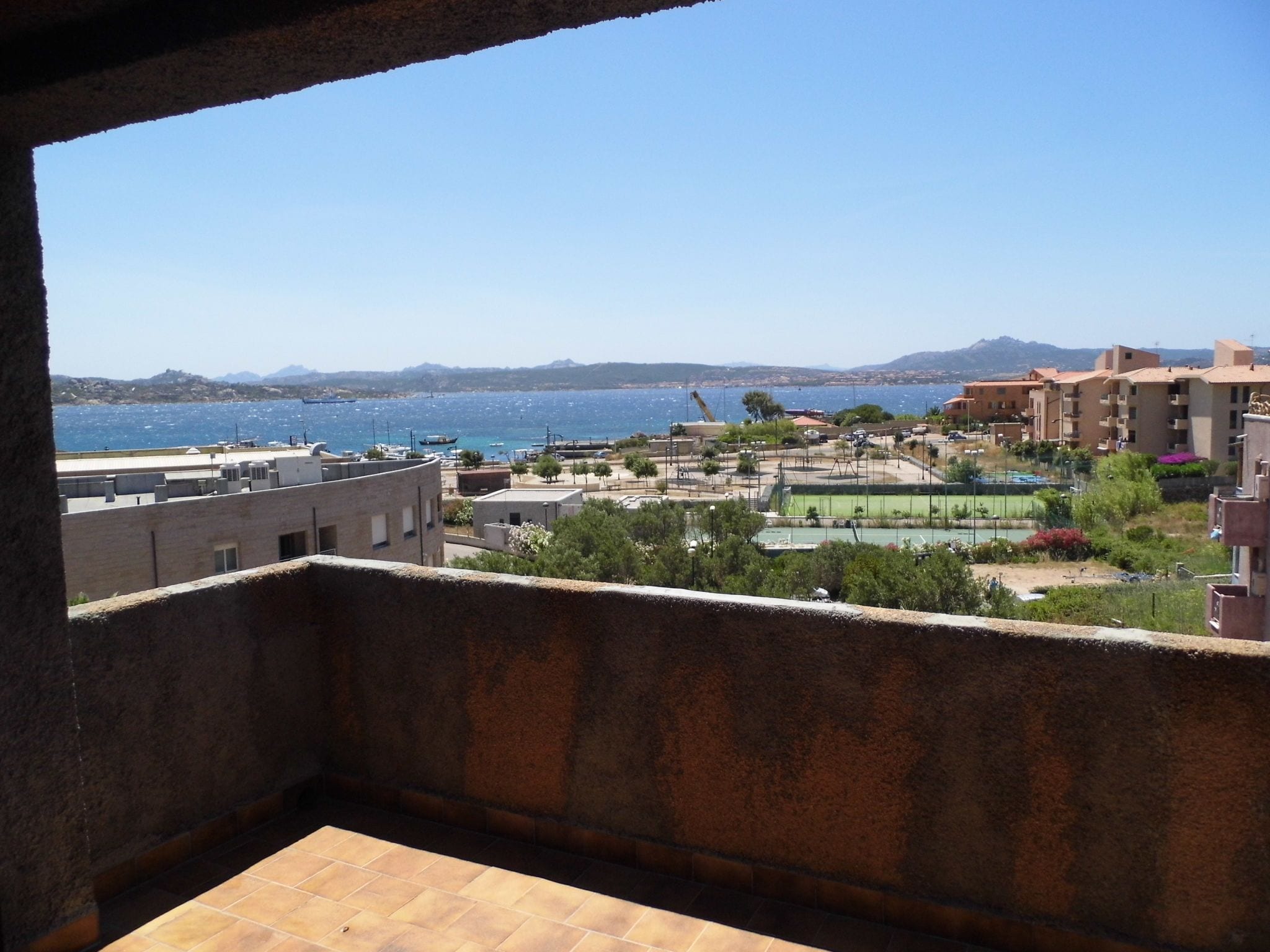 A balcony with a view of a coastal area, including buildings, a sports field, and the sea.