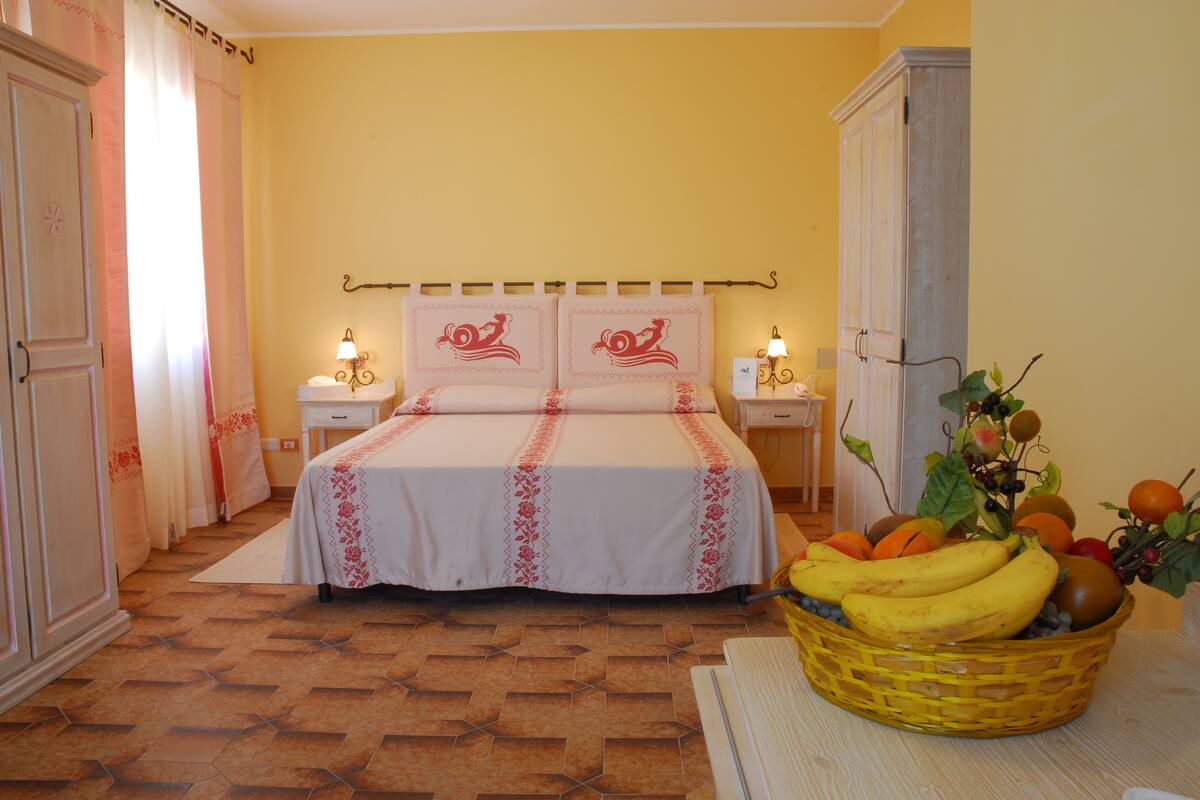 Un dormitorio con una cama, mesitas de noche, una lámpara, una cesta de frutas y un armario.