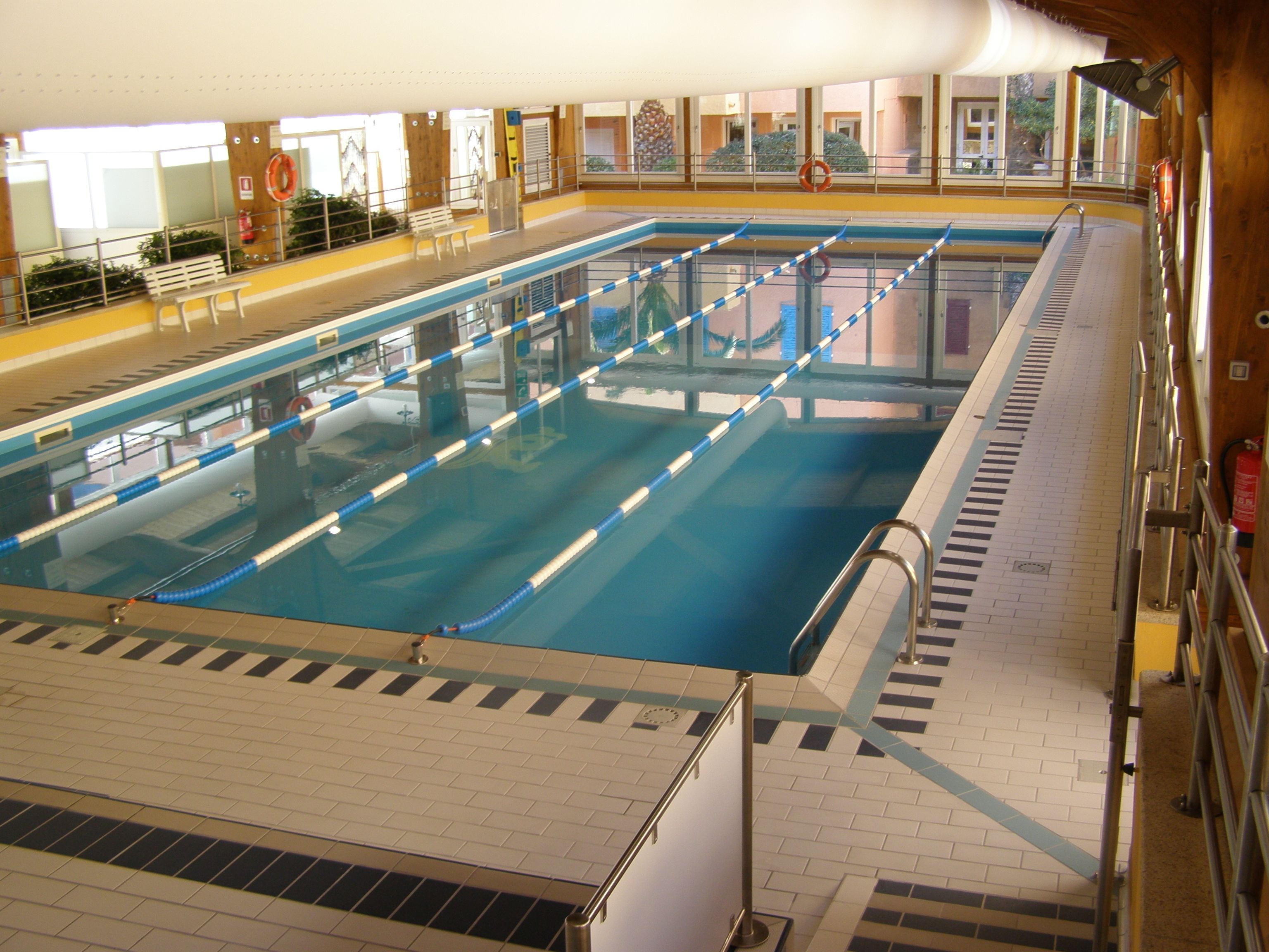 Une piscine intérieure avec des lignes de démarcation bien visibles, un sol carrelé et des rampes de sécurité.
