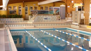 Una piscina interior amb separadors de carrils ben definits, una zona de solàrium enrajolada i un sostre de fusta.
