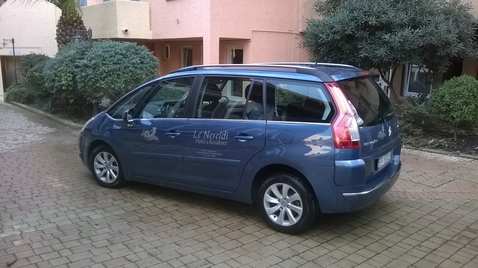 Un coche familiar azul estacionado en un camino de entrada pavimentado.