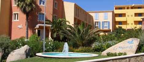 A hotel with a stone fountain, palm trees, and a sign reading "Le Nereidi".