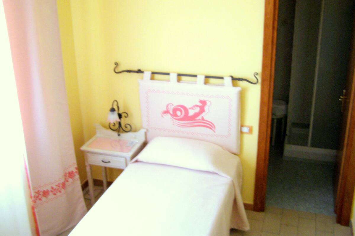 Un dormitorio pequeño y ordenado con una cama individual, una mesita de noche y una mesilla.