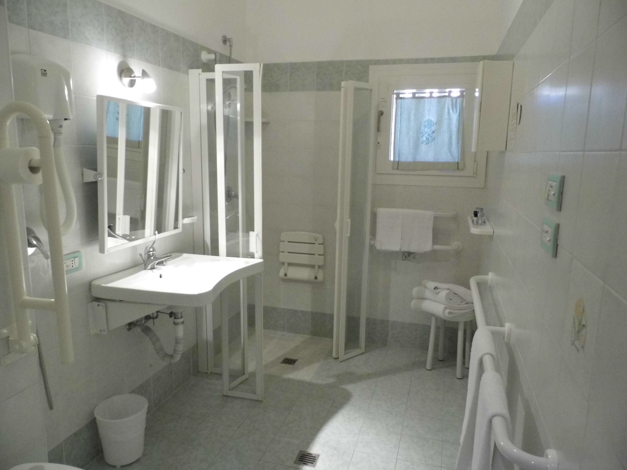 A modern bathroom with a shower enclosure, a sink, a toilet, and a window with a curtain.