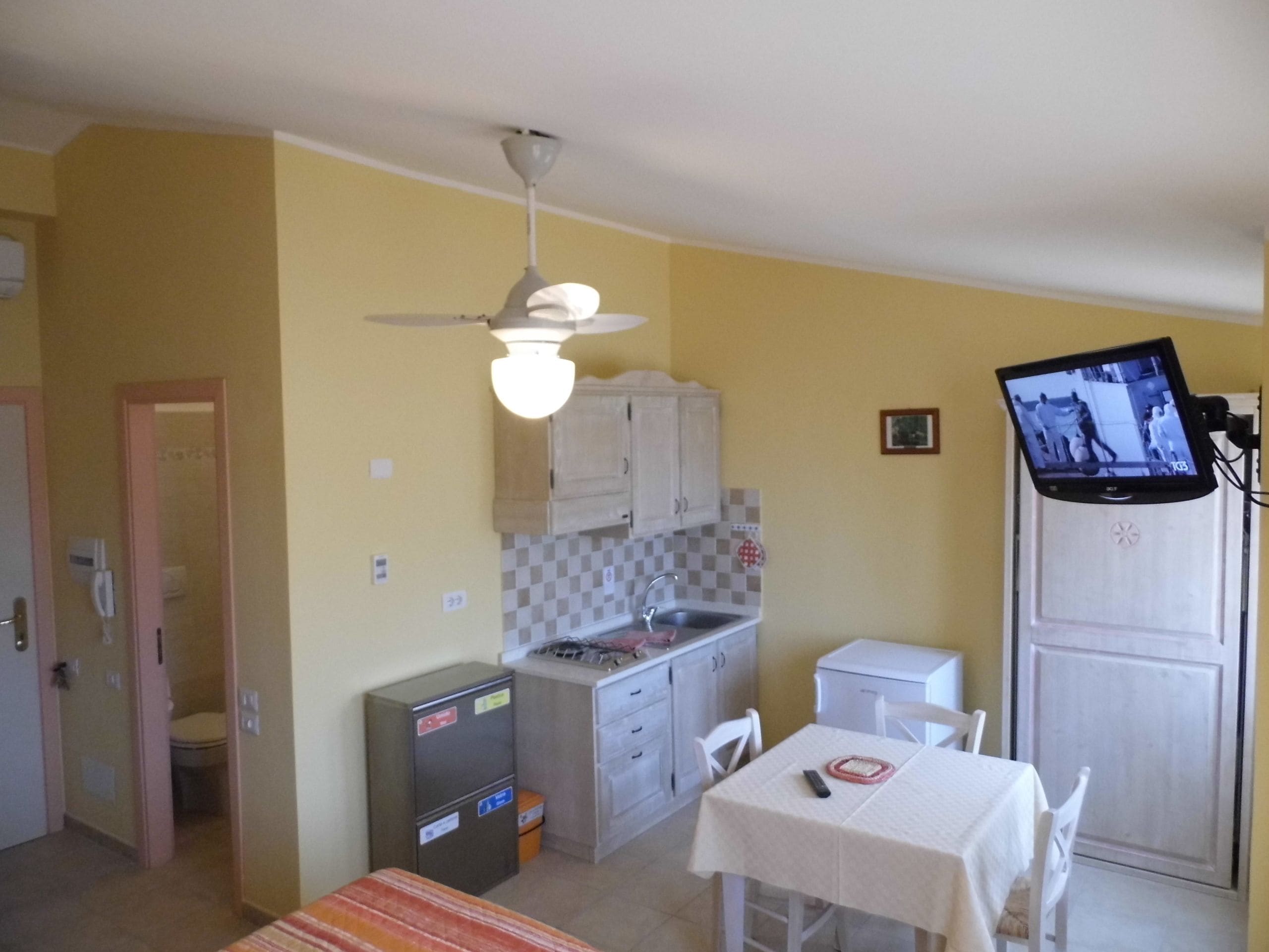 Una cucina compatta con zona pranzo, una ventola a soffitto e un televisore montato a parete.
