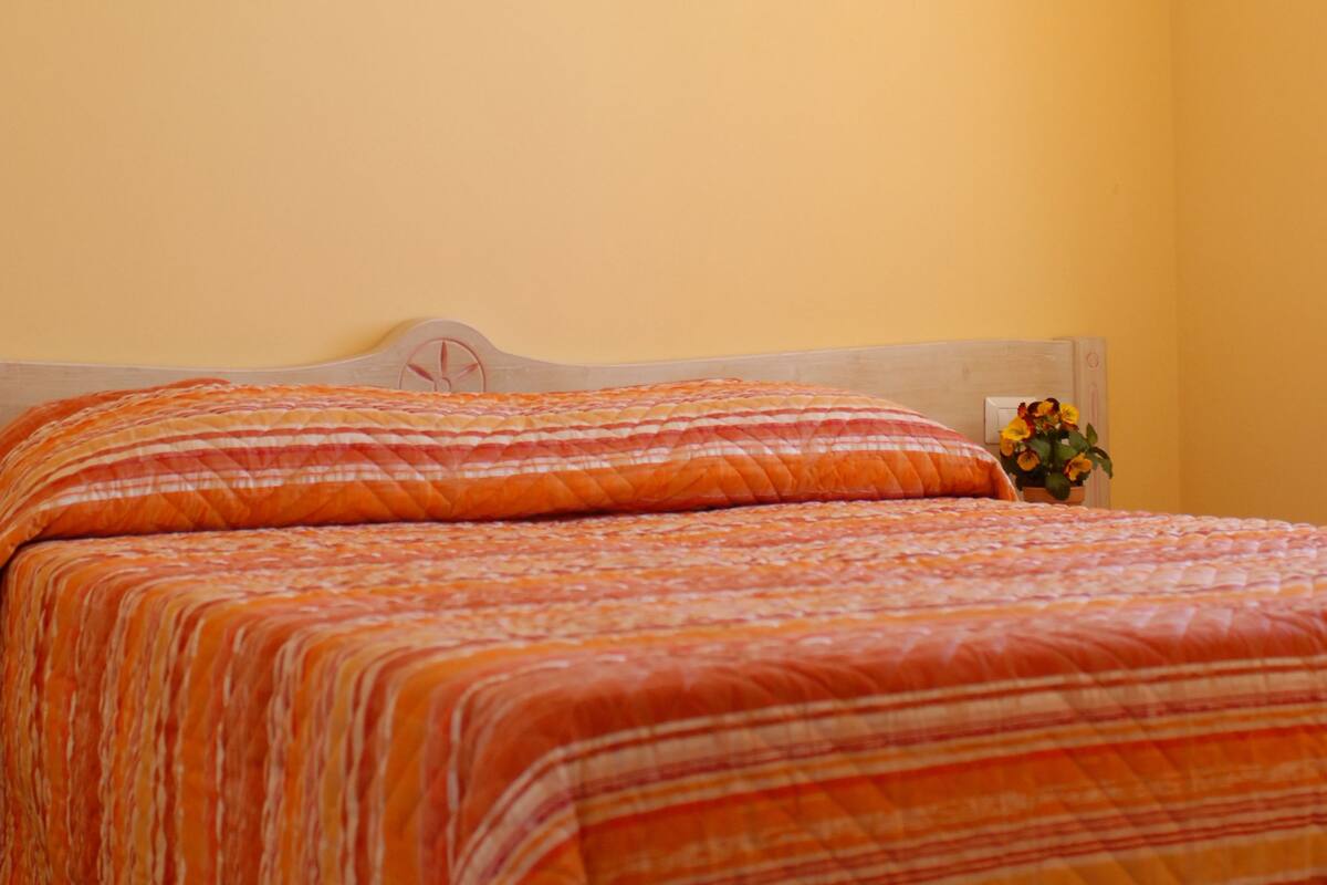Una habitación con dos camas, un ventilador de techo y un pequeño florero con flores.