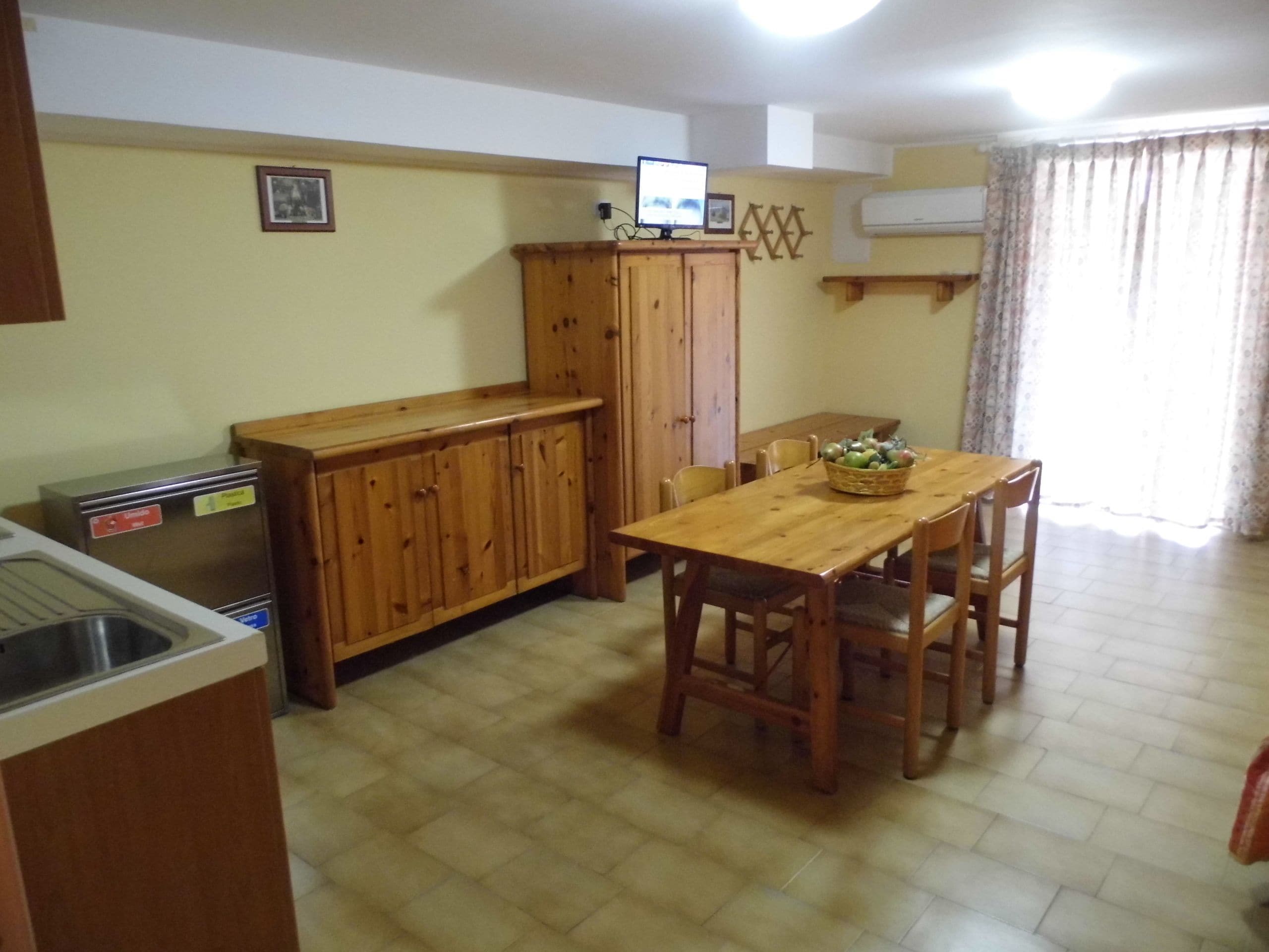 A compact kitchen with a wooden table, chairs, a refrigerator, and a wooden cabinet.