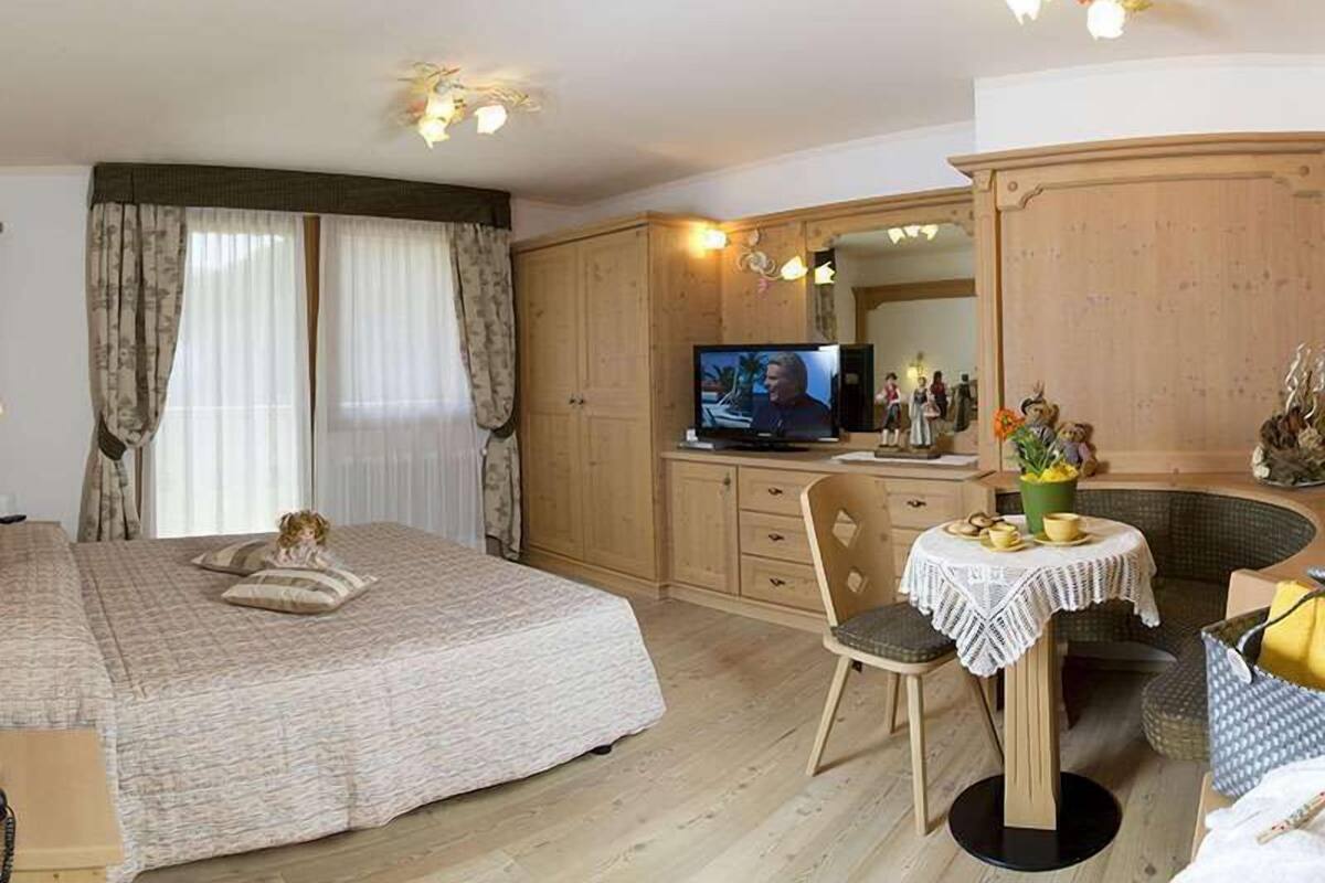 Un dormitorio con una cama, un televisor, una mesita con una silla y un armario.
