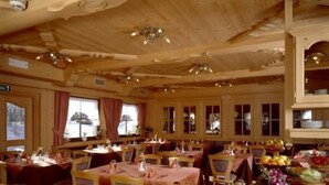 Un interior de madera con varias mesas dispuestas para una comida, sillas y una vajilla ordenada.