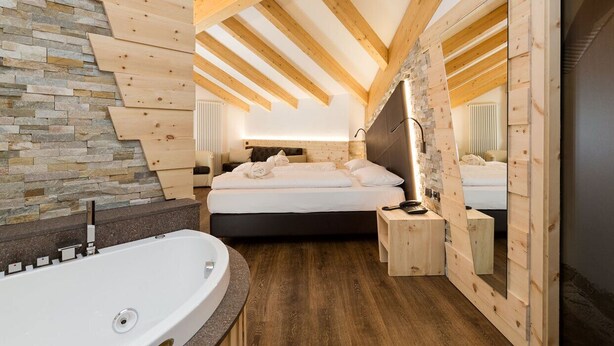 Un dormitorio moderno con una cama grande, techo de madera, pared de piedra y una bañera.