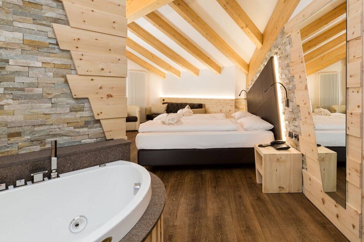 Un dormitorio moderno con una cama grande, techo de madera, pared de piedra y una bañera.